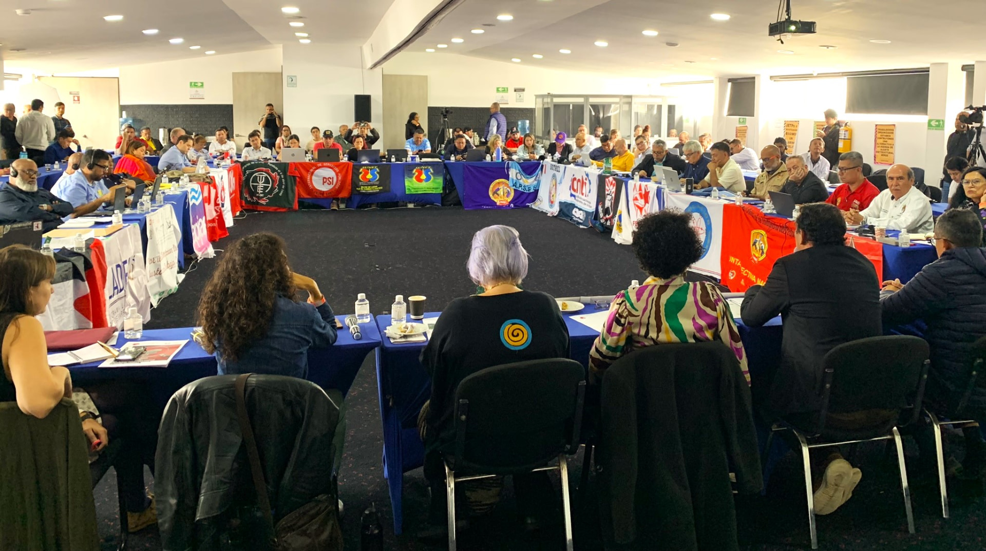 Delegates seated around a large circular table covered with union banners at a TUED Latin America meeting