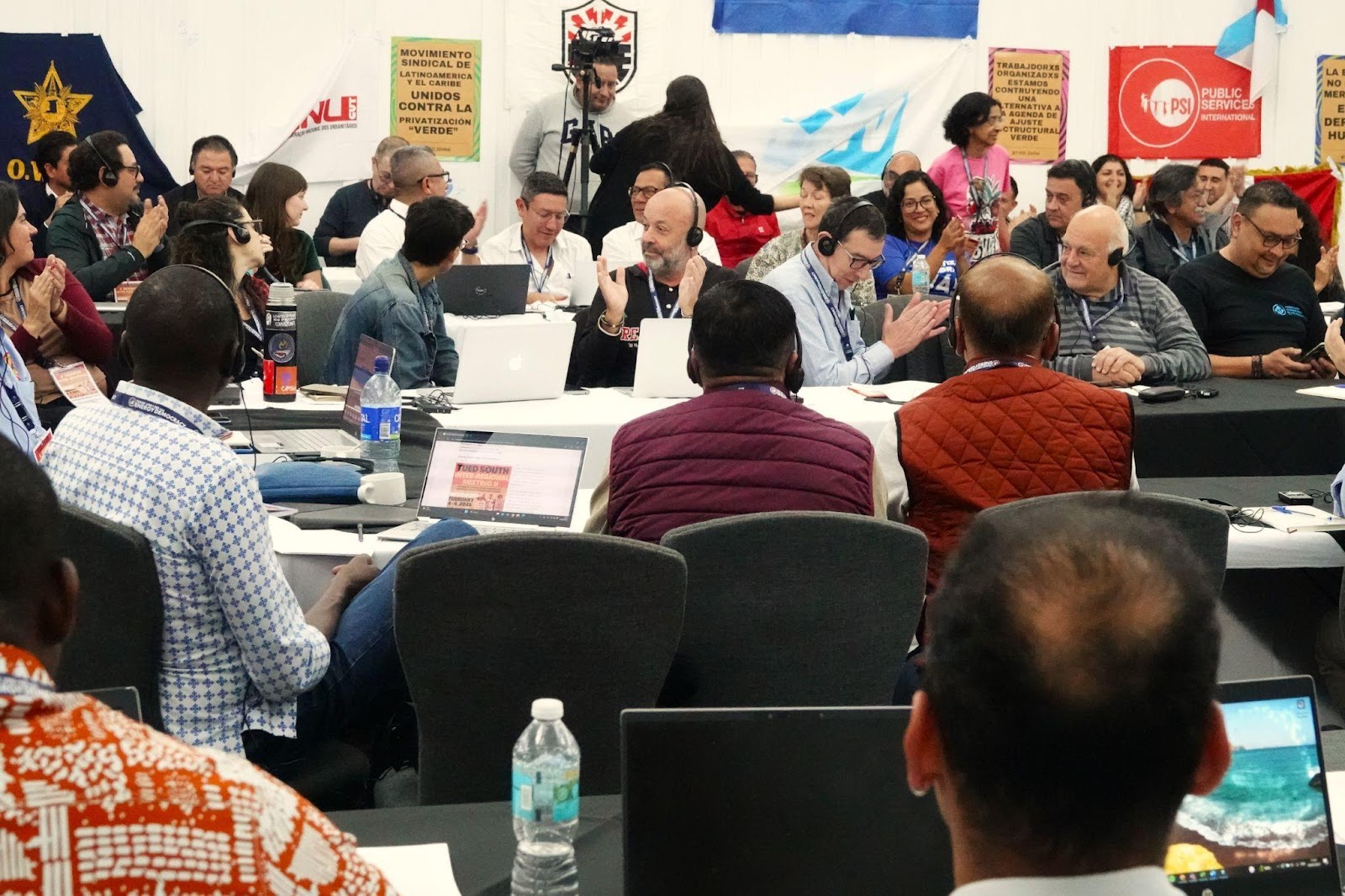 Delegates applauding during a TUED meeting session with PSI and Latin American union banners behind them