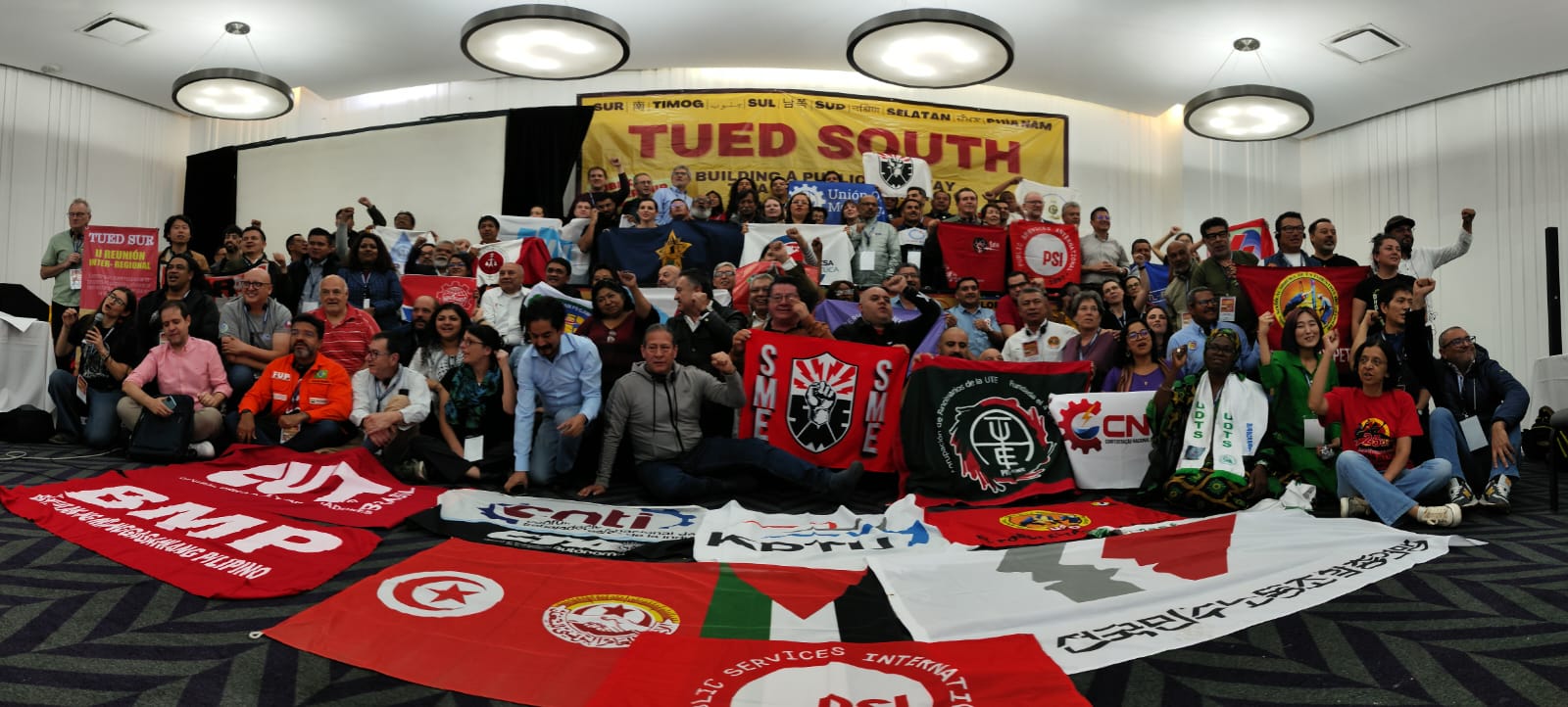 Large group shot of TUED delegates from across the Americas holding union banners and flags at the TUED South meeting in Mexico City