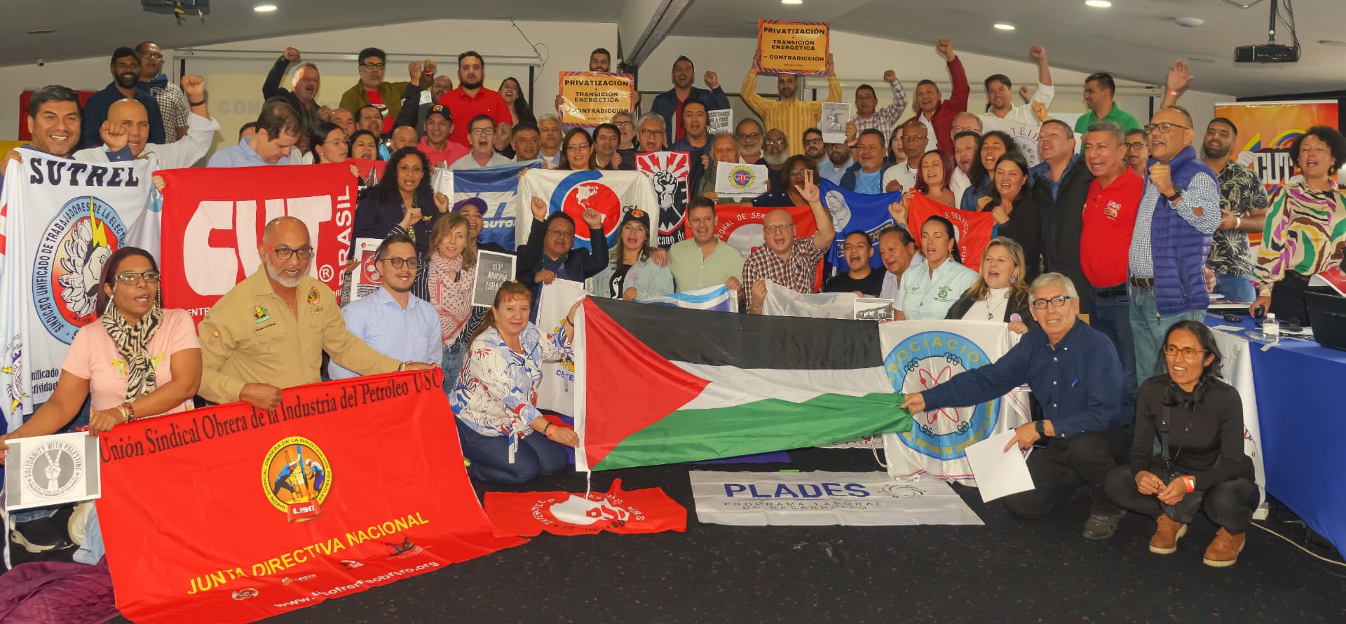 Latin American trade unionists posing with union banners and the Palestinian flag at a TUED regional meeting